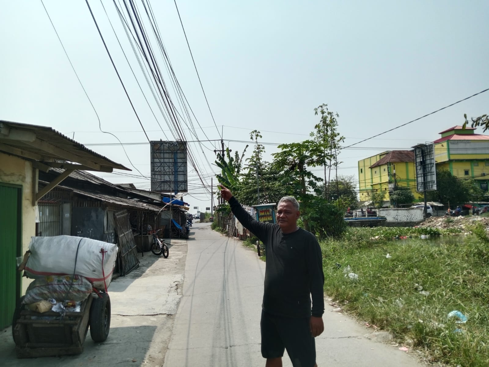 Caption : Kepala Dusun Warudoyong Utara, Muktar, menunjukkan kondisi kabel jaringan telekomunikasi yang menjuntai rendah dan semrawut di RT 33/RW 07, Desa Rengasdengklok Selatan, Kecamatan Rengasdengklok, Kabupaten Karawang. Warga meminta pihak terkait segera melakukan penataan dan perbaikan karena dinilai berpotensi membahayakan keselamatan pengguna jalan dan masyarakat sekitar. (Foto: Patriotjabar.com/Mir)