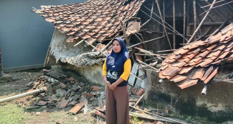 Caption : Ibu Sarwi berdiri di depan rumahnya yang roboh di Dusun Jatiboros RT 15/RW 05, Desa Kertajaya, Kecamatan Jayakerta, Kabupaten Karawang. Enam bulan pascakejadian akibat hujan deras disertai angin kencang, keluarga masih terpaksa menumpang di rumah kerabat sambil berharap adanya bantuan renovasi dari Pemerintah Kabupaten Karawang. (Foto: Gugun/Patriotjabar.com) Caption : Ibu Sarwi berdiri di depan rumahnya yang roboh di Dusun Jatiboros RT 15/RW 05, Desa Kertajaya, Kecamatan Jayakerta, Kabupaten Karawang. Enam bulan pascakejadian akibat hujan deras disertai angin kencang, keluarga masih terpaksa menumpang di rumah kerabat sambil berharap adanya bantuan renovasi dari Pemerintah Kabupaten Karawang. (Foto: Gugun/Patriotjabar.com)