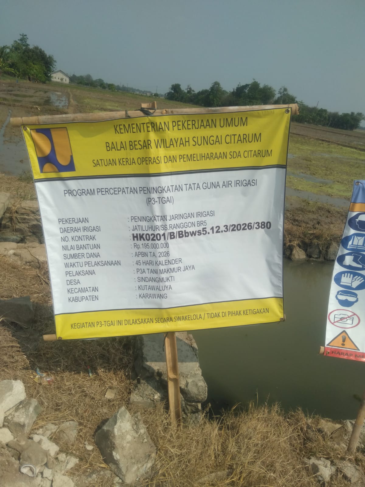 Caption : Papan informasi proyek P3-TGAI di Desa Sindangmukti, Kecamatan Kutawaluya, Kabupaten Karawang. Proyek peningkatan jaringan irigasi yang dilaksanakan oleh P3A Tani Makmur Jaya dengan nilai bantuan Rp195 juta dari APBN Tahun Anggaran 2026 tersebut menjadi sorotan publik menyusul dugaan pelaksanaan pekerjaan yang tidak sesuai spesifikasi teknis pasangan batu.