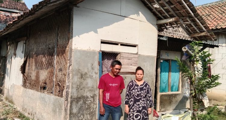Caption : Suryadi bersama istrinya berdiri di depan rumah mereka yang kondisinya sangat memprihatinkan di Dusun Tegalasem, RT 14/RW 06, Desa Kertasari, Kecamatan Rengasdengklok, Kabupaten Karawang. Dinding bilik yang lapuk, atap yang rusak, serta struktur bangunan yang nyaris roboh membuat keluarga tersebut hidup dalam kekhawatiran. Mereka berharap Pemerintah Kabupaten Karawang segera merealisasikan bantuan melalui program Rumah Tidak Layak Huni (Rutilahu). (Foto: Gunawan/Patriotjabar.com)