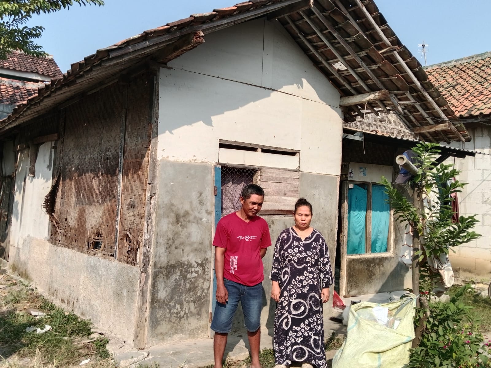 Caption : Suryadi bersama istrinya berdiri di depan rumah mereka yang kondisinya sangat memprihatinkan di Dusun Tegalasem, RT 14/RW 06, Desa Kertasari, Kecamatan Rengasdengklok, Kabupaten Karawang. Dinding bilik yang lapuk, atap yang rusak, serta struktur bangunan yang nyaris roboh membuat keluarga tersebut hidup dalam kekhawatiran. Mereka berharap Pemerintah Kabupaten Karawang segera merealisasikan bantuan melalui program Rumah Tidak Layak Huni (Rutilahu). (Foto: Gunawan/Patriotjabar.com) Caption : Suryadi bersama istrinya berdiri di depan rumah mereka yang kondisinya sangat memprihatinkan di Dusun Tegalasem, RT 14/RW 06, Desa Kertasari, Kecamatan Rengasdengklok, Kabupaten Karawang. Dinding bilik yang lapuk, atap yang rusak, serta struktur bangunan yang nyaris roboh membuat keluarga tersebut hidup dalam kekhawatiran. Mereka berharap Pemerintah Kabupaten Karawang segera merealisasikan bantuan melalui program Rumah Tidak Layak Huni (Rutilahu). (Foto: Gunawan/Patriotjabar.com)