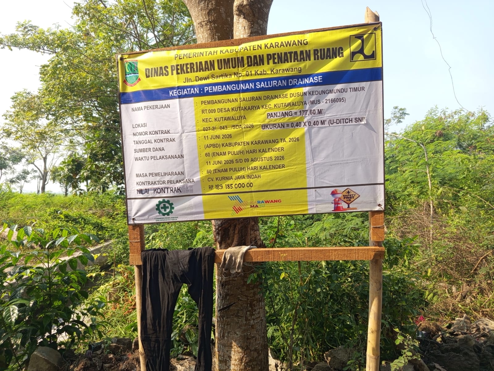 Caption : Papan informasi proyek pembangunan saluran drainase U-Ditch di Dusun Kedungmundu Timur, Desa Kutakarya, Kecamatan Kutawaluya, Kabupaten Karawang. Proyek yang dikerjakan oleh CV Kurnia Jaya Indah dengan nilai kontrak Rp189.185.000 bersumber dari APBD Kabupaten Karawang Tahun Anggaran 2026 tersebut menjadi sorotan terkait dugaan minimnya penerapan standar Keselamatan dan Kesehatan Kerja (K3) di lapangan.