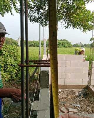 Caption: Pekerja tengah melakukan pekerjaan konstruksi pembangunan toilet SMPN 2 Jayakerta, Karawang. Terlihat pengukuran jarak pemasangan besi menggunakan meteran pada bagian struktur bangunan yang menjadi sorotan terkait dugaan ketidaksesuaian spesifikasi teknis.
